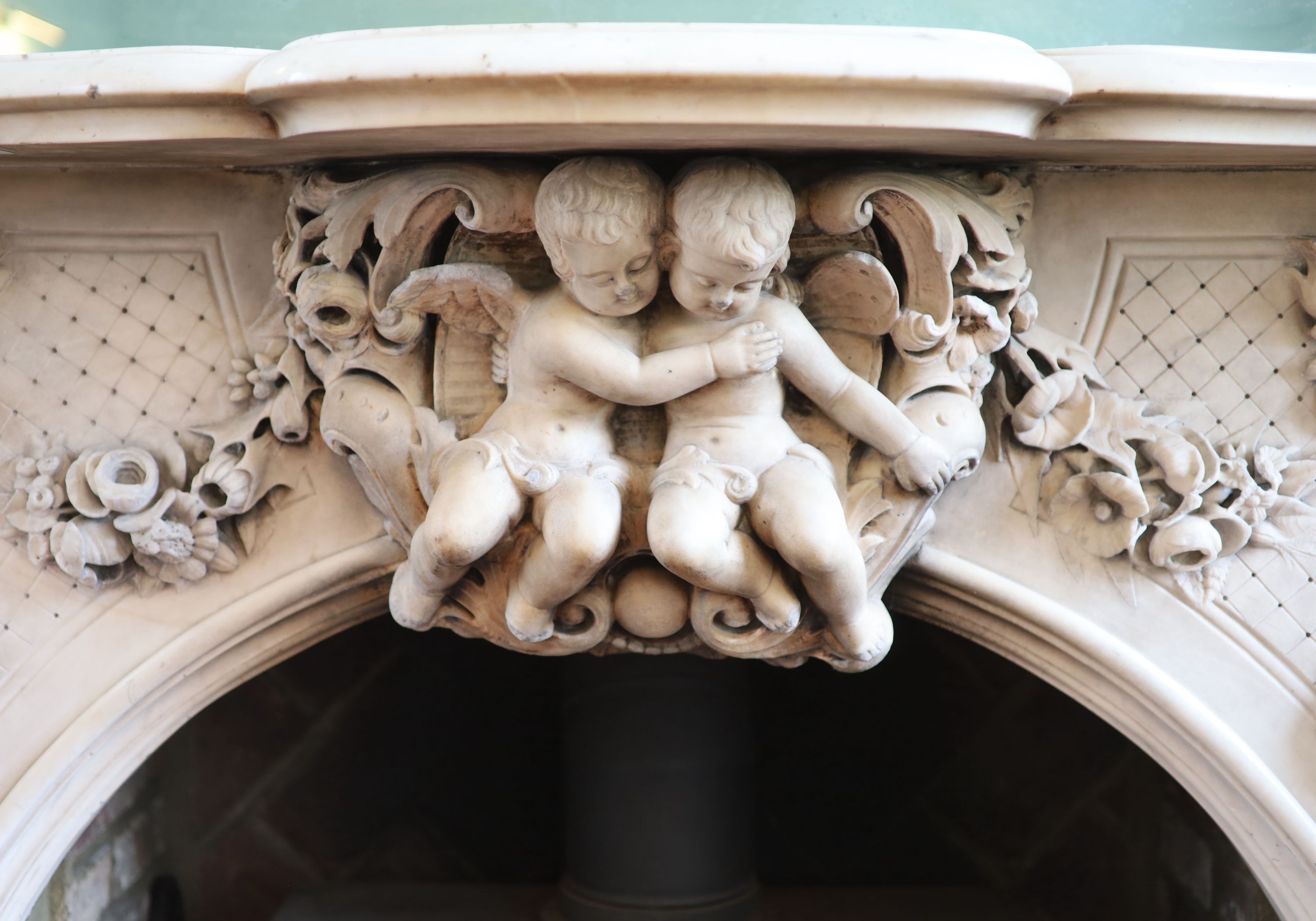 An important mid 19th century Italian white Carrara marble chimney piece, carved in the rococo taste, with seated putti, foliage swags